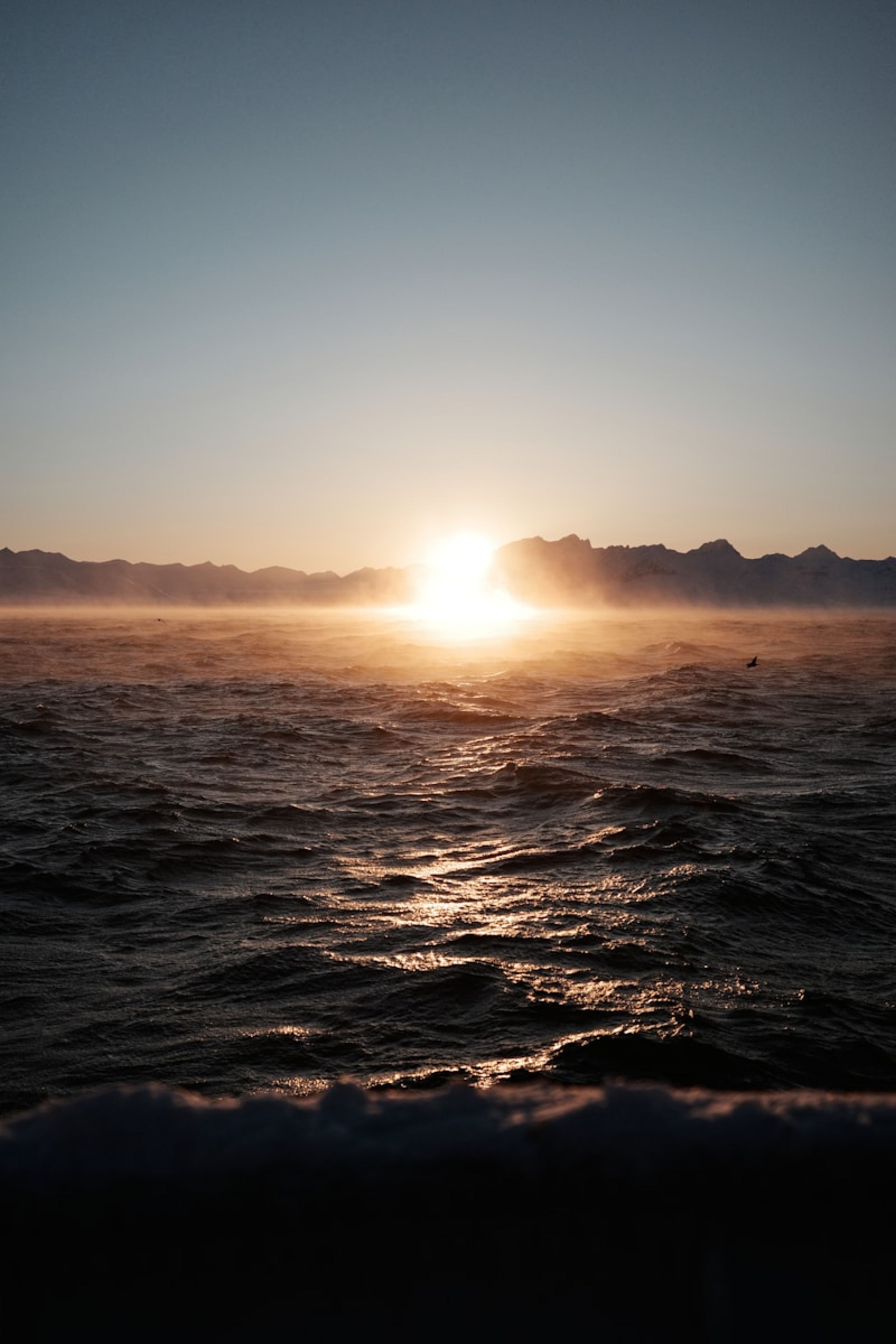 The sun is setting over the ocean with mountains in the distance