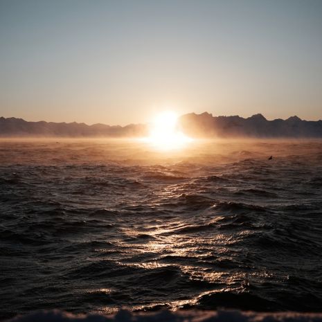 The sun is setting over the ocean with mountains in the distance